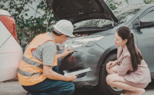 Homem inspeciona a frente de um carro com o capô aberto enquanto uma mulher observa ao lado