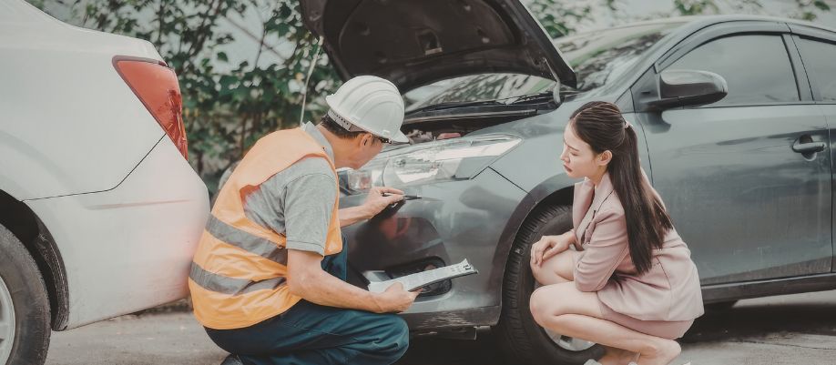 Homem inspeciona a frente de um carro com o capô aberto enquanto uma mulher observa ao lado
