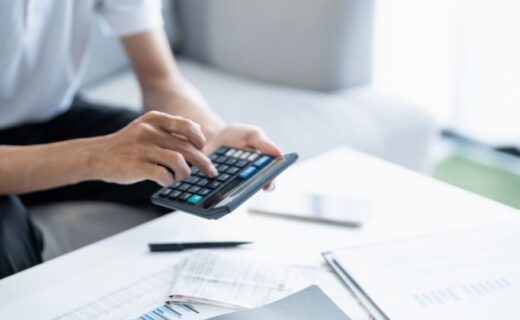 Pessoa usando calculadora ao lado de documentos sobre a mesa, em contexto de organização financeira