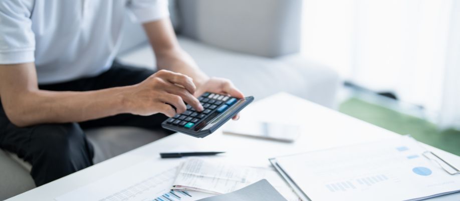 Pessoa usando calculadora ao lado de documentos sobre a mesa, em contexto de organização financeira