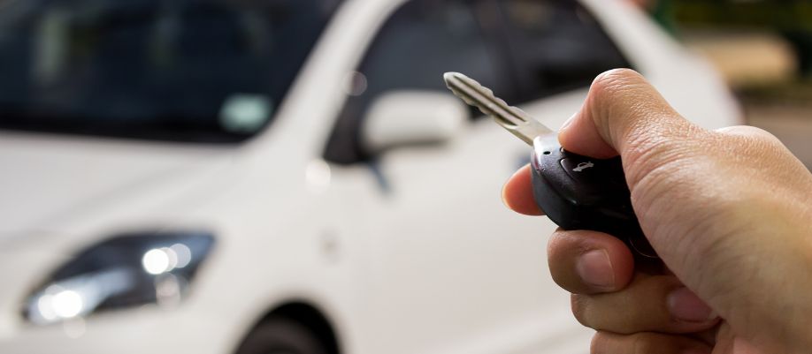 Mão segurando a chave de um carro branco ao fundo, em imagem ilustrativa sobre veículo de repasse