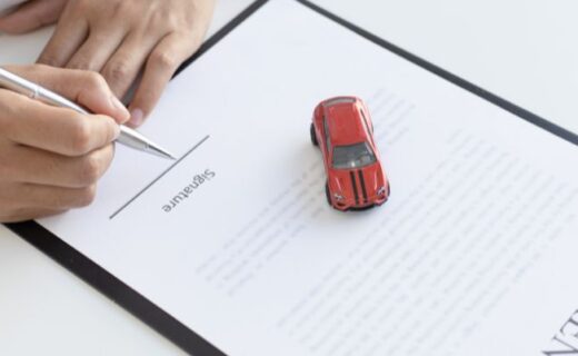 Mãos assinando um documento ao lado de um carrinho vermelho sobre a mesa