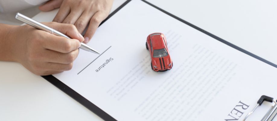 Mãos assinando um documento ao lado de um carrinho vermelho sobre a mesa